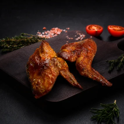 Alitas de pollo bañadas en salsa BBQ sobre tabla de madera con tomillo