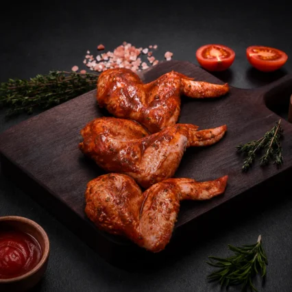 Alitas de pollo marinadas en salsa BBQ sobre tabla de madera con tomate
