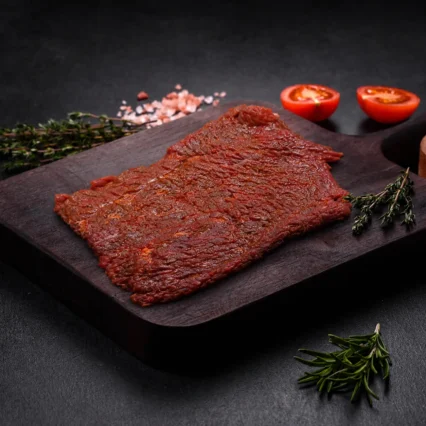 Bistec de res marinado en salsa BBQ sobre tabla de madera con tomate