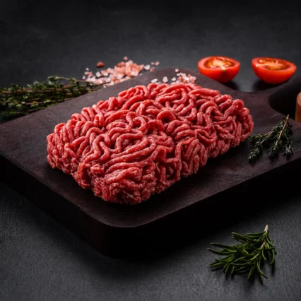 Carne molida especial fresca sobre tabla de madera con tomate y tomillo