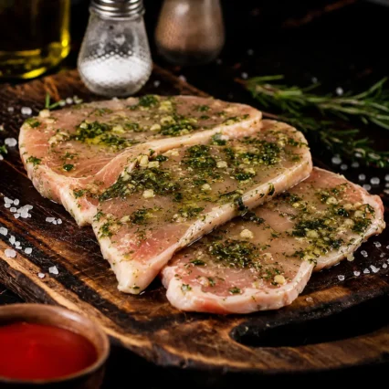 Chuletas de cerdo marinadas al ajillo sobre tabla de madera con romero