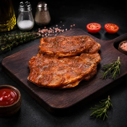 Chuletas de cerdo marinadas en salsa BBQ sobre tabla de madera con tomate