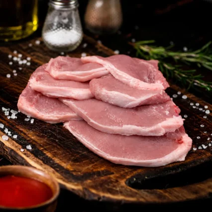 Chuleta riñonada de cerdo en tabla oscura con sal en grano y romero
