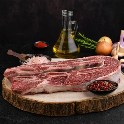 Costilla de res cruda sobre tabla de madera con especias y aceite de oliva