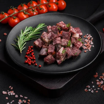 Morcilla cortada en cubos sobre plato negro con romero y sal rosada