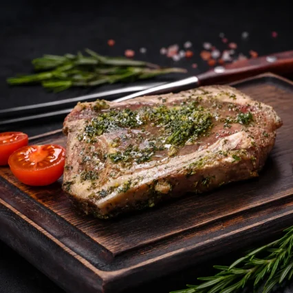 Corte de T-Bone marinado al ajillo sobre tabla de madera con tomate