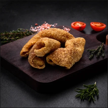 Chicharrones de cerdo dorados y crujientes sobre tabla de madera con tomate