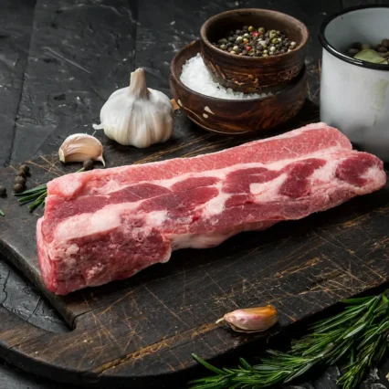 Costillar de cerdo fresco sobre tabla de madera con ajo, romero y especias