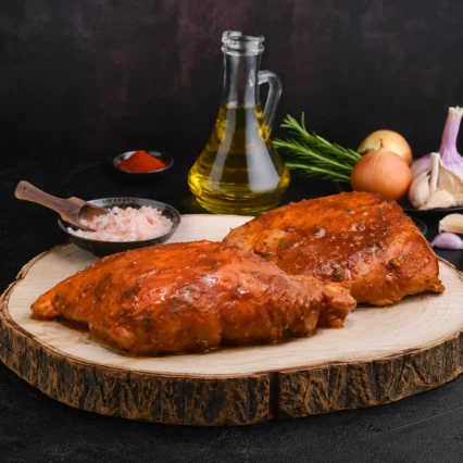 Filetes de pechuga de pollo marinados en salsa BBQ sobre tabla de madera rústica