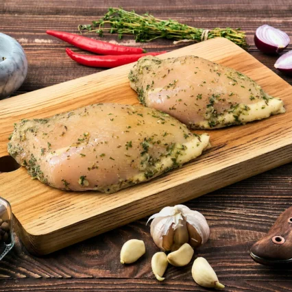 Pechugas de pollo marinadas al ajillo sobre tabla de madera con ajo