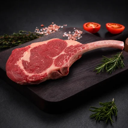 Corte de Tomahawk con hueso largo sobre tabla de madera con tomate