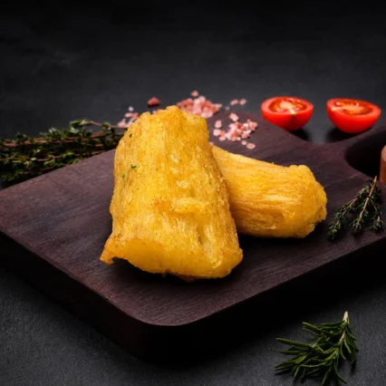 Trozos de yuca frita y dorada sobre tabla de madera con tomate
